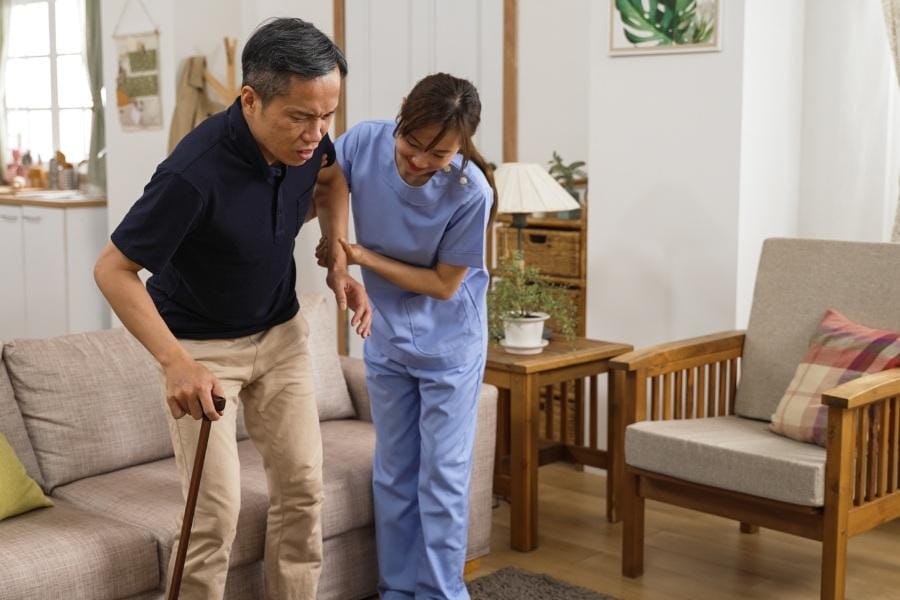 RN helping her client walk across the living room