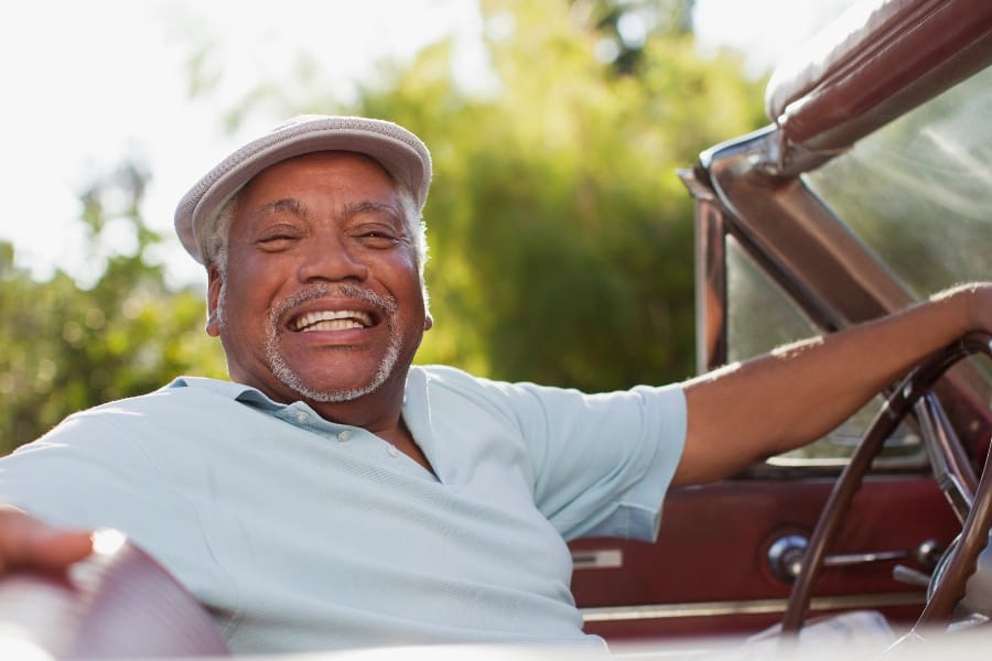 A senior citizen smiling in his classic car